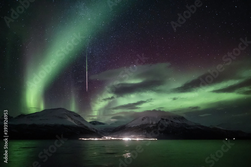 Northern lights and a shooting star above snow-covered mountains by the sea