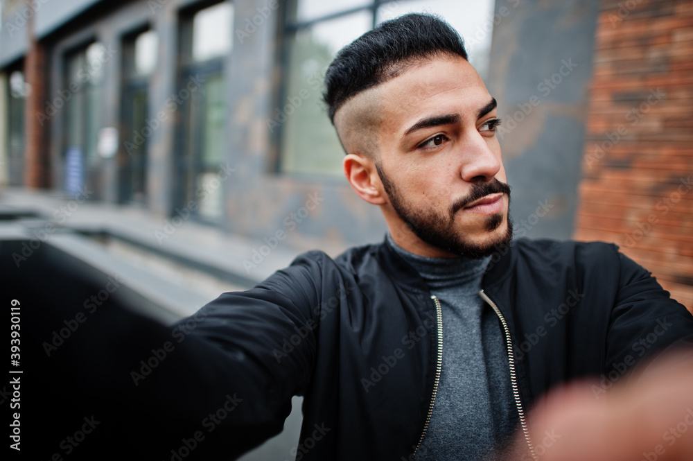 Obraz premium Portrait of stylish arab beard man wear grey turtleneck and black jaket. Arabian model guy make selfie by camera.