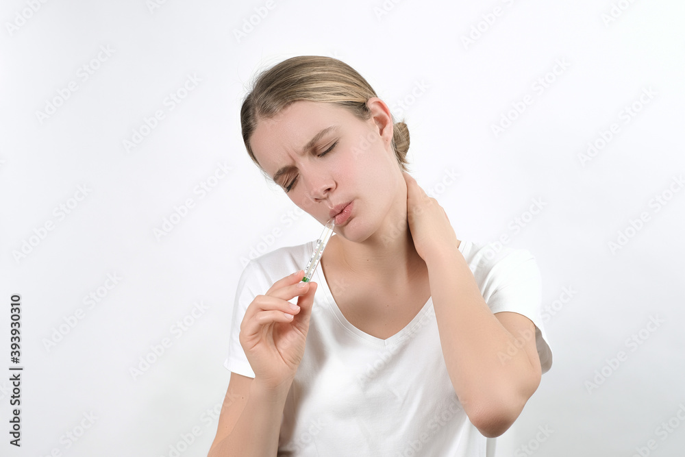 young caucasian blonde woman holding a thermometer in her mouth and keeping raised hand on her head and frowning sadly face, isolated on the white background. Flu high fever virus. young caucasian blonde woman holding a thermometer in her mouth and keeping raised hand on her head and frowning sadly face, isolated on the white background. Flu high fever virus.