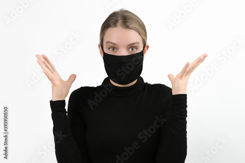 confused young girl shrugging shoulders, making helpless gesture with hands, throws up her hands in confusion wearing face mask on the white background in the studio