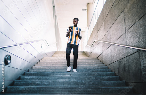 фотографія Stylish black man walking downstairs and messaging on cellphone