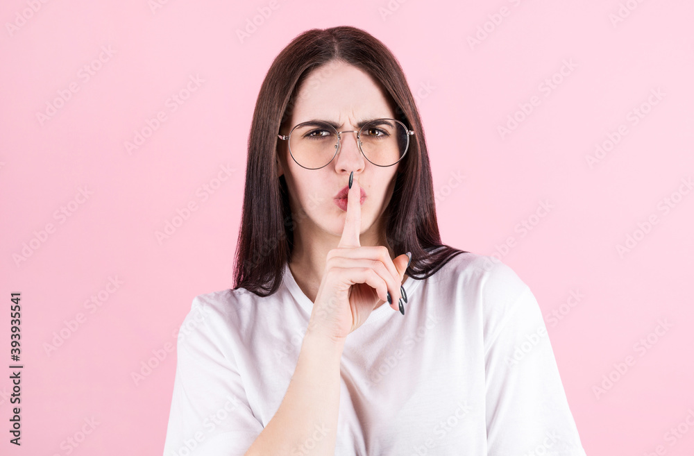 American woman presses index finger to lips, asks be quiet, tells very private information, wears casual yellow vest, poses in studio, says shush or hush American woman presses index finger to lips, asks be quiet, tells very private information, wears casual yellow vest, poses in studio, says shush or hush