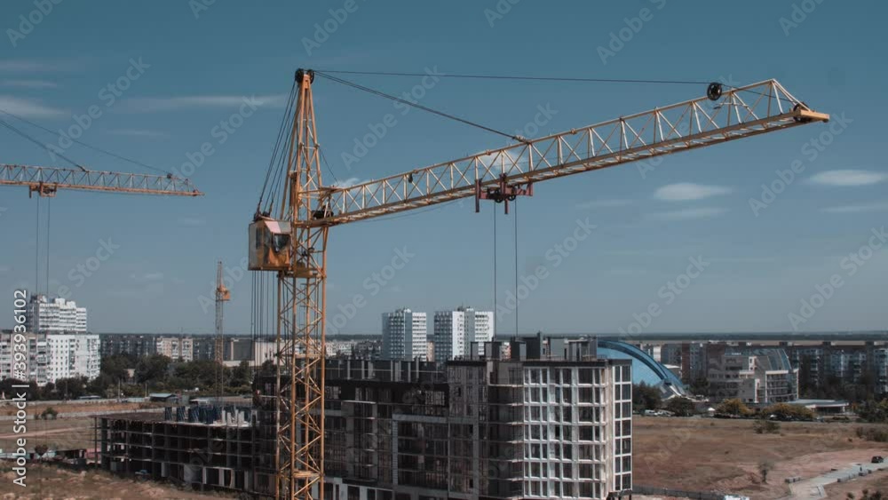 Aerial view of moving constructor crane from a drone. Quiet town on a background and new modern buildings Aerial view of moving constructor crane from a drone. Quiet town on a background and new modern buildings