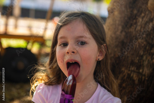 beautiful little girl eating a grape ice cream on a stick