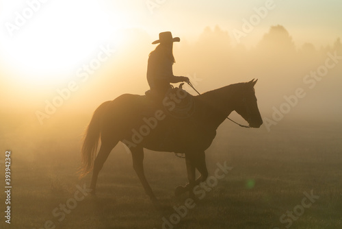 silhouette of cowgirl with lasso on horse at sunrise