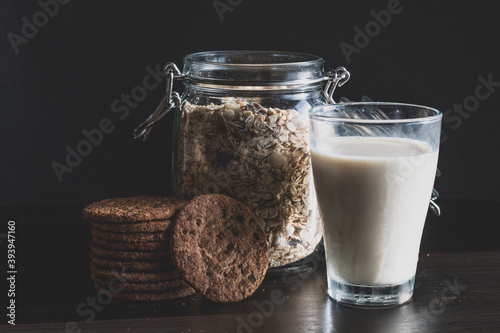 Serving healthy morning breakfast with corn flakes Whole grains muesli, fresh milk in a glass and Pile of Delicious Chocolate homemade Chip Cookies on a vintage dark background. Aesthetic composition