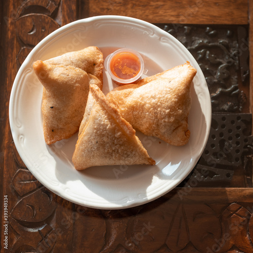 Samosas on a wooden table served with hot red sauce on white porcelain