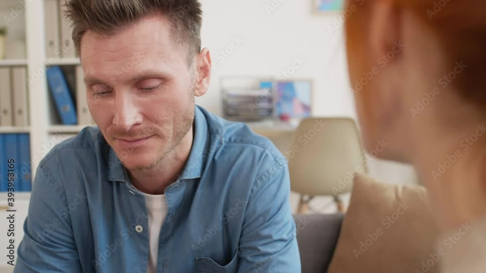 Close-up over shoulder of unrecognizable red-haired female psychologist listening to male middle-aged Caucasian patient sitting in medical office, speaking out and drinking water Close-up over shoulder of unrecognizable red-haired female psychologist listening to male middle-aged Caucasian patient sitting in medical office, speaking out and drinking water