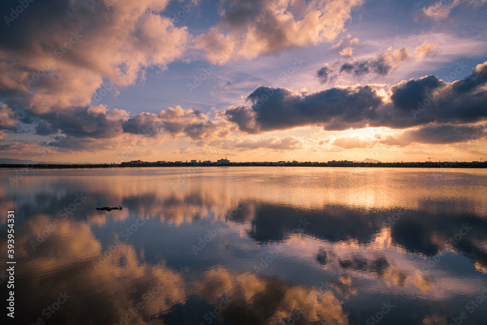 Reflection on the water of a salt lake of a beautiful sunset with a sky full of clouds in Regional Park of the Salinas and Arenales de San Pedro del Pinatar, Murcia, Spain