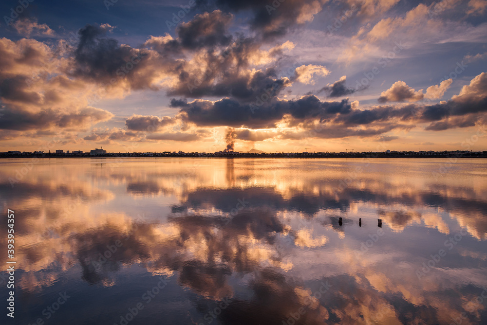 Reflection on the water of a salt lake of a beautiful sunset with a sky full of clouds in Regional Park of the Salinas and Arenales de San Pedro del Pinatar, Murcia, Spain