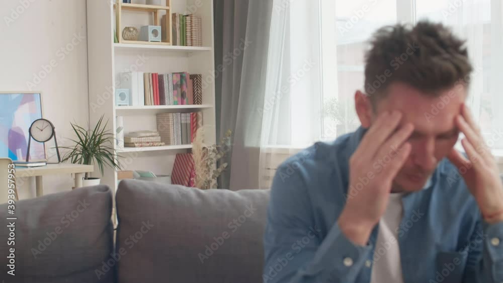 Medium close-up of middle-aged Caucasian man sitting on couch in office rubbing face, unrecognizable person giving him book, he reading Medium close-up of middle-aged Caucasian man sitting on couch in office rubbing face, unrecognizable person giving him book, he reading