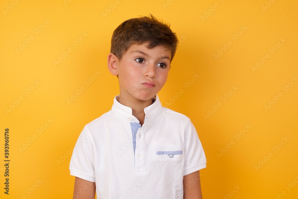 little cute Caucasian boy kid wearing white t-shirt against yellow wall, looks pensively aside, plans actions after university, imagines what to do Thinks over about new project. little cute Caucasian boy kid wearing white t-shirt against yellow wall, looks pensively aside, plans actions after university, imagines what to do Thinks over about new project.