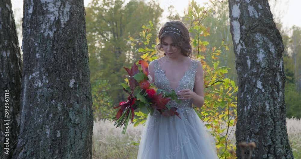 A young woman dressed in a gray wedding dress celebrates her wedding. She has flowers in her hand and is in the park. A young woman dressed in a gray wedding dress celebrates her wedding. She has flowers in her hand and is in the park.
