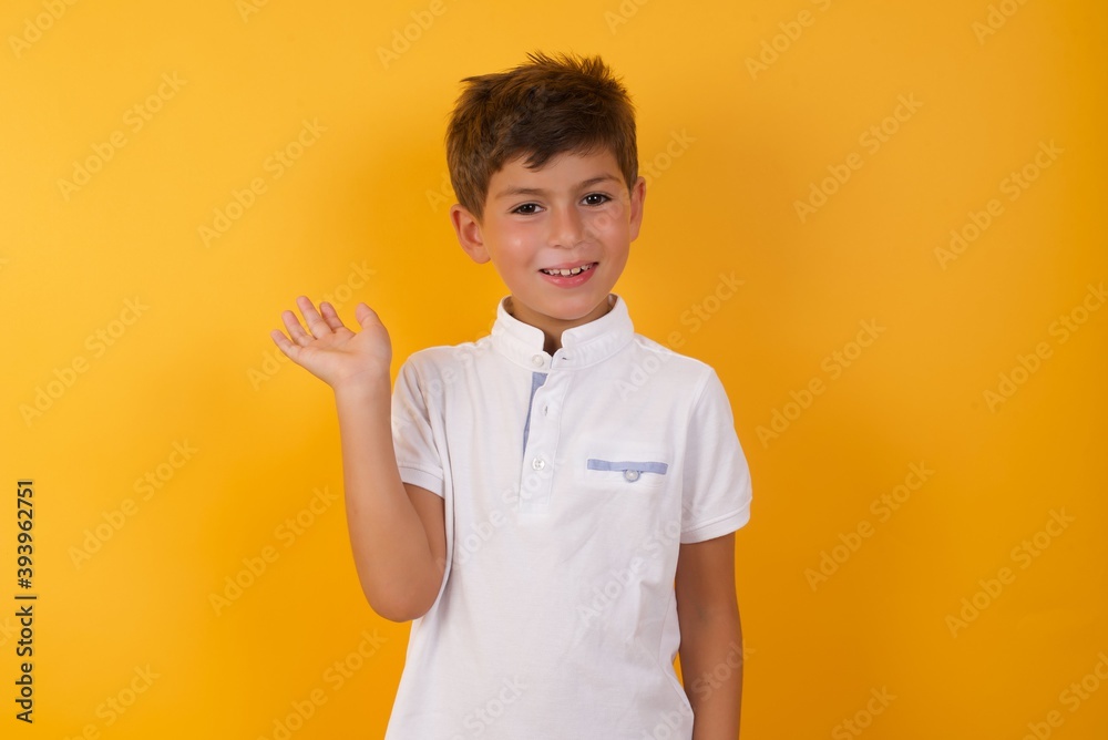 Positive glad little cute boy kid wearing white t-shirt against yellow wall says: wow how exciting it is, has amazed expression, shows something on blank space with open hand. Advertisement concept. Positive glad little cute boy kid wearing white t-shirt against yellow wall says: wow how exciting it is, has amazed expression, shows something on blank space with open hand. Advertisement concept.