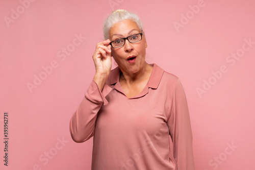 Fotografía Surprised senior woman looking through glasses otices something unexpected,