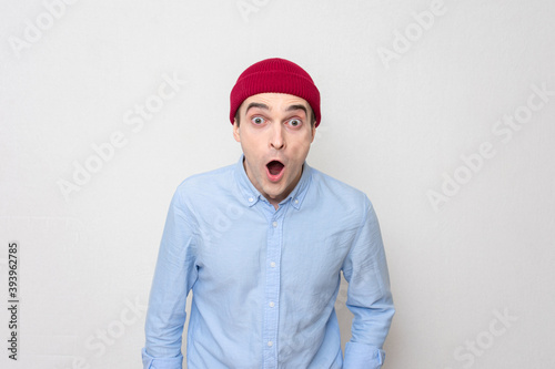 Surprised guy in a red cap and blue shirt looks at the camera, portrait