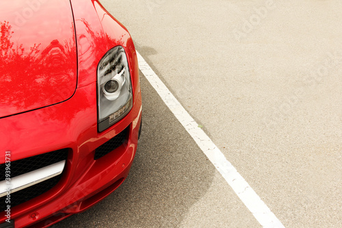 The front of a red car on a background of asphalt. Car headlights. Luxury Headlights