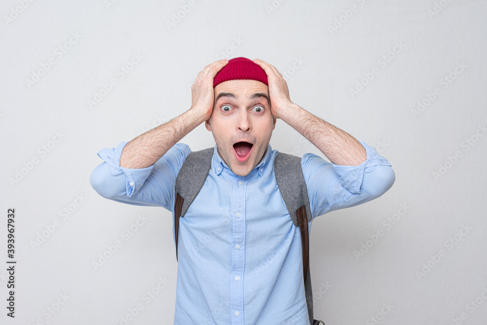 Shocked student with a backpack and a red hat looks at the camera, white background, portrait Shocked student with a backpack and a red hat looks at the camera, white background, portrait