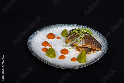 Tuna steak covered with broccoli and decorations on white plate and black background