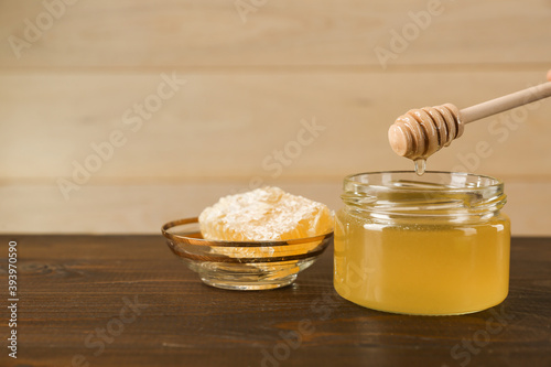 honey flowing from honey dipper into the jar on wooden background in rustic style