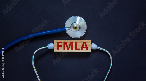 Wooden block with word 'FMLA, family medical leave act' and stethoscope on black background. Medical concept. Copy space.