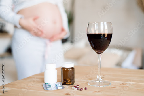 A glass of red wine and pills on the background of a pregnant woman. Alcoholic concept. © nagaets