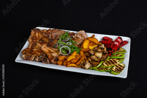 Big meat plate with potatoes and vegetables on black background