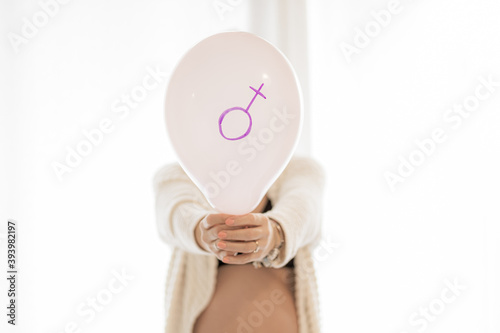 A pregnant woman is holding a pink balloon - Young pregnant girl is behind and taking in the hand the balloon during maternity time
