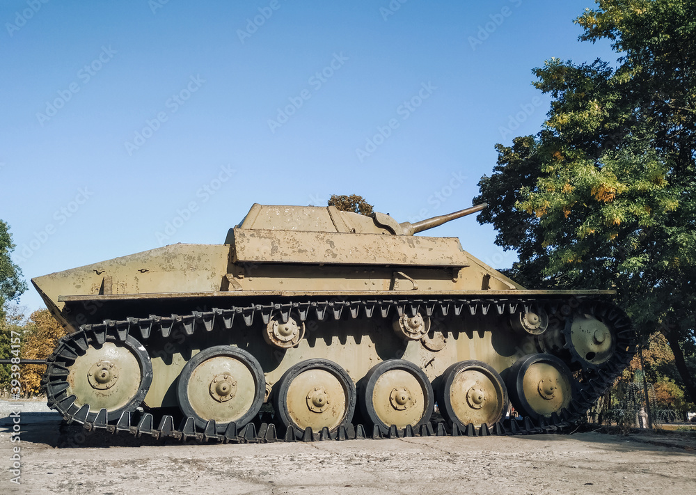 An old Soviet model of the T-70 tank stands against the background of trees and sky. Light armored military equipment of the USSR.