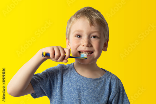 a boy with white hair holds a toothbrush in his hands wants to brush his teeth. yellow background.