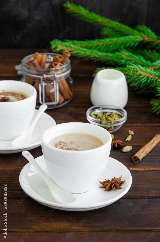 Hot tea with milk, cinnamon, cardamom, anise and other spices, Indian masala tea in a white cup on a wooden background. copy space.