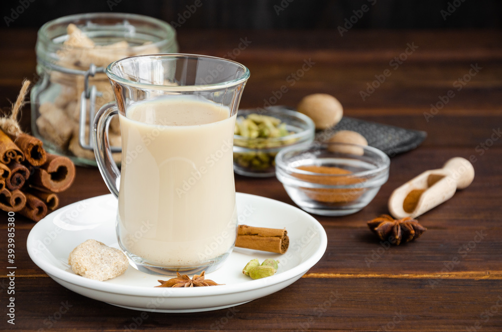 Hot tea with milk, cinnamon, cardamom, anise and other spices, Indian masala tea in a glass cup on a wooden background. copy space. Hot tea with milk, cinnamon, cardamom, anise and other spices, Indian masala tea in a glass cup on a wooden background. copy space.
