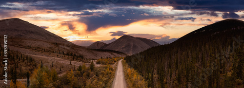 Panoramic View of Scenic Road from Above surrounded by Mountains and Forest. Dramatic Colorful Sunset Sky. Aerial Drone Shot. Taken near the Dempster Highway, Yukon, Canada.