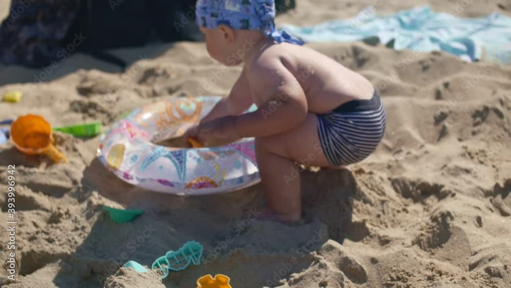 Chubby baby in bandana playing with sand on the beach using molds. Chubby baby in bandana playing with sand on the beach using molds.