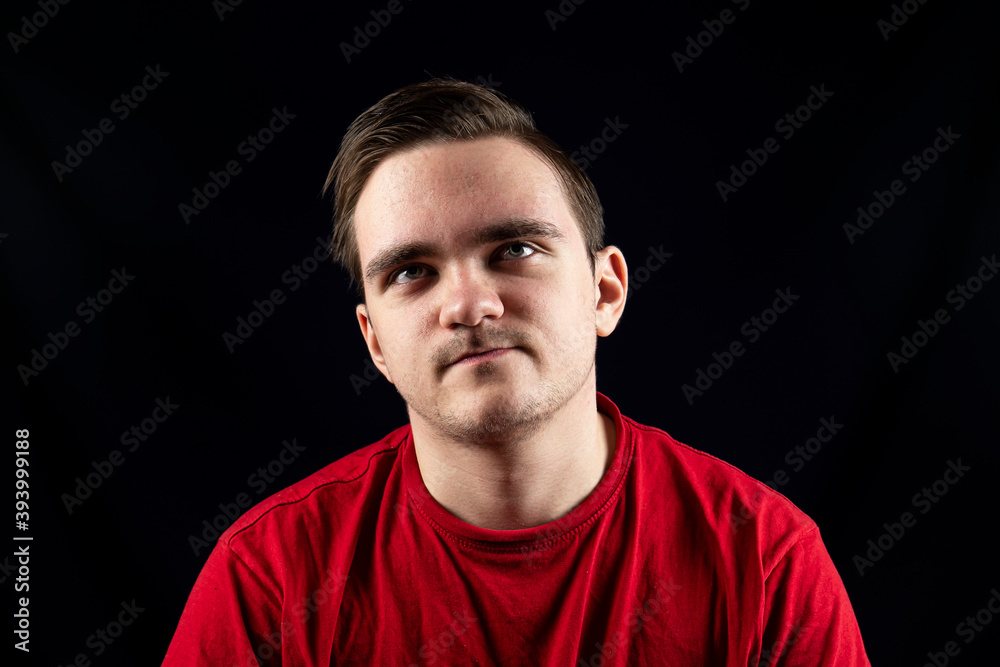 Young man in casual t-shirt standing against isolated dark background Young man in casual t-shirt standing against isolated dark background