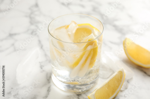 Soda water with lemon slices and ice cubes on white marble table