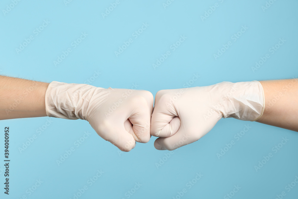 People in medical gloves doing fist bump on light blue background, closeup of hands