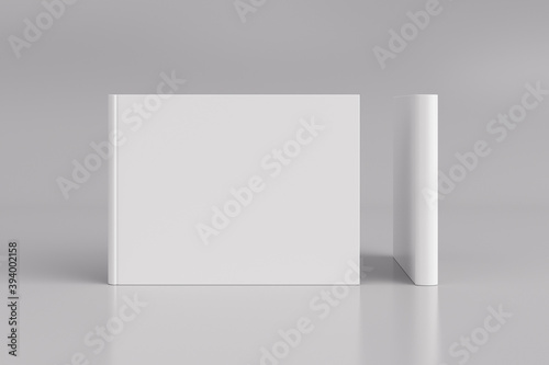 Two hardcover horizontal or landscape white mockup books standing on the white background. Blank front cover and spine of book. © dimamoroz