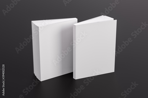 Two softcover or paperback vertical white mockup books standing on the black table. Blank front and back cover. photo