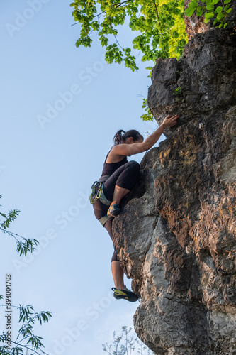 happy beautiful caucasian woman with long brown hair rock climbing, flexing her muscles on a sunny day in the mountains, strongly holding on to cliffs. Healthy outdoor sports and activities in nature