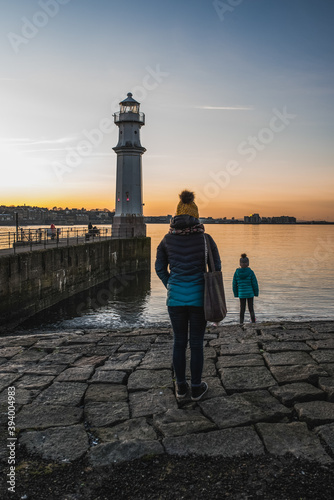 Family standing in front of the sea with a lighthouse in the background at sunset. photo