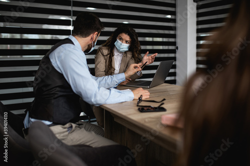 Business people working together in their office on important project. They are talking and analyzing their business plan together. They wearing protective face masks against virus infection.