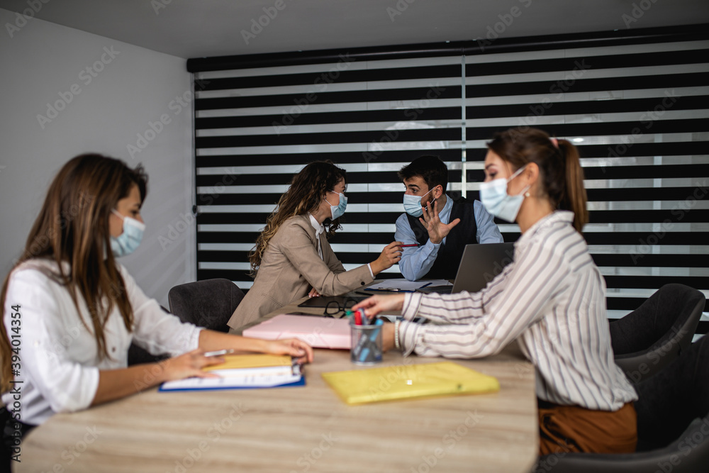 Fototapeta premium Group of four business people working together are talking and analyzing their business plan. They wearing protective face masks against virus infection.