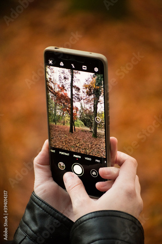 A hand holding an mobile Phone trying to capture the awesome colors of autumn in the forest