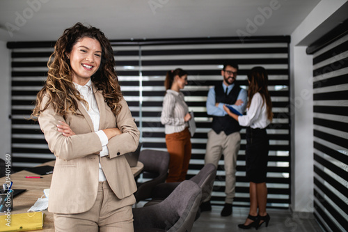 Group of four business people working together in their office on important project. One successful and happy woman standing in front, posing and looking at camera.