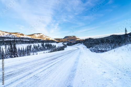 Long snow covered road in Yukon territories with snow coved mountains in back ground and frozen lake to the sid