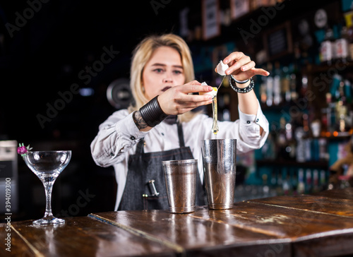 Young woman tapster decorates colorful concoction at the night club