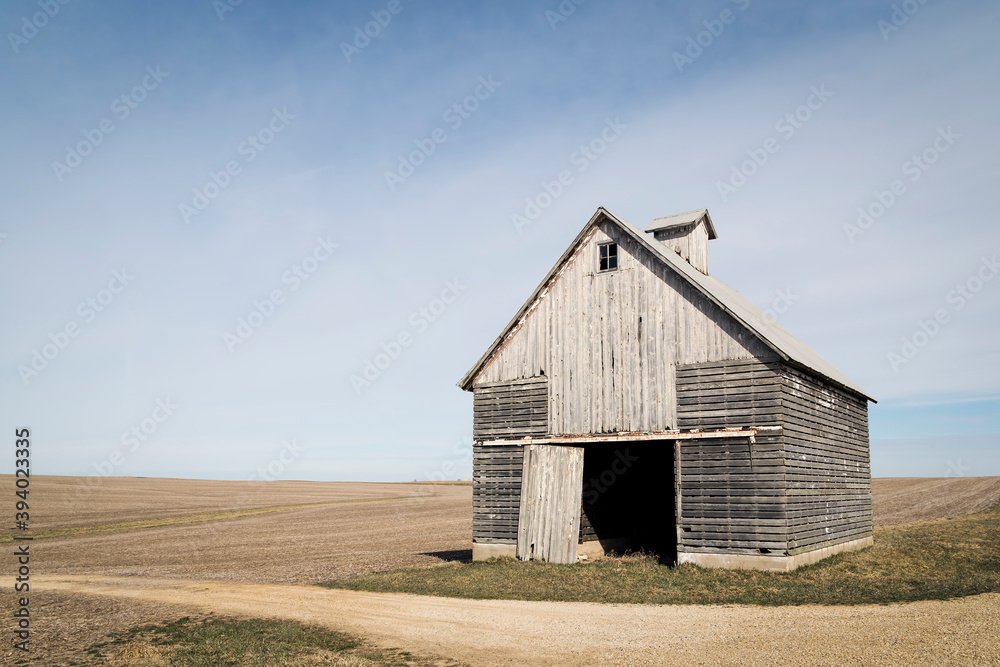 An Old Corn Crib by a Rural Gravel Road stands before an Open Farm Field