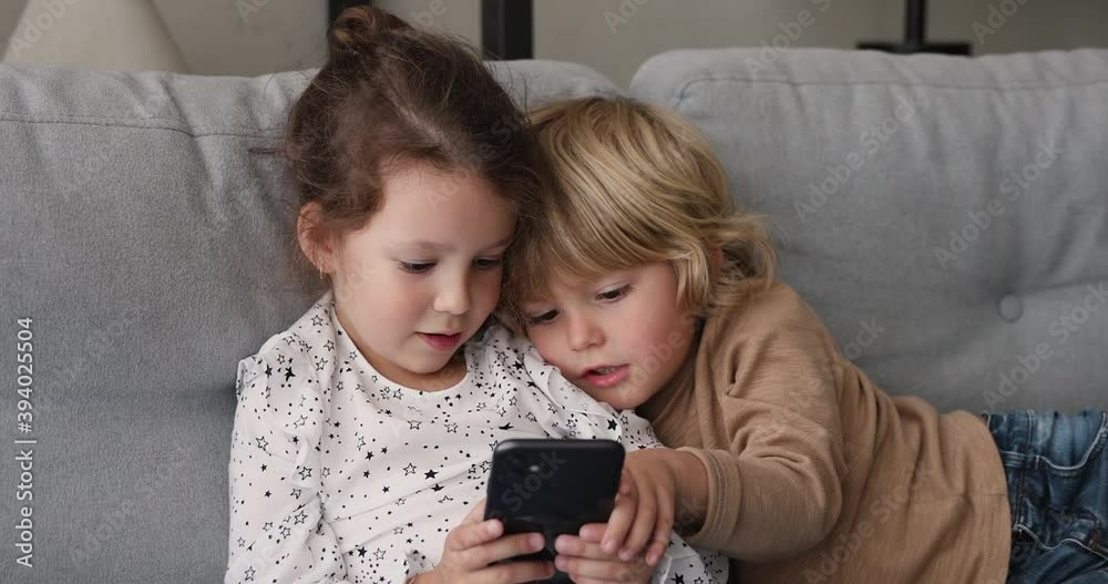 Close up five years old girl and boy resting on couch using smartphone, play games, watch cartoons, having fun on internet. Bad habit, new generation addicted with modern digital technologies concept Close up five years old girl and boy resting on couch using smartphone, play games, watch cartoons, having fun on internet. Bad habit, new generation addicted with modern digital technologies concept