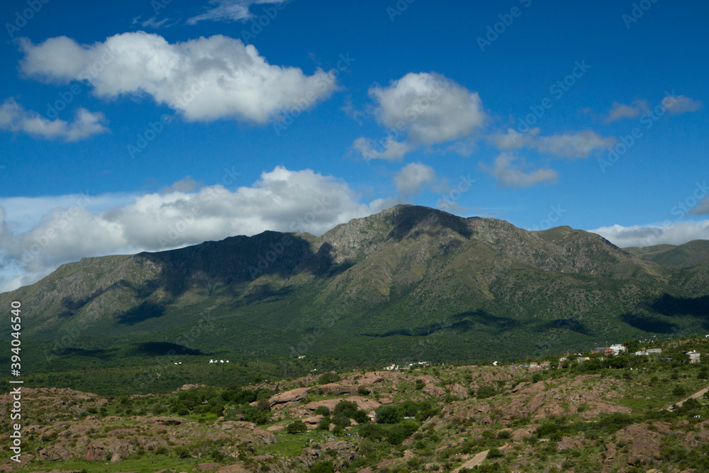Fototapeta premium Beautiful view of popular landmark Uritorco hill, valley and green forest under a deep blue sky with clouds in Capilla del Monte, Cordoba, Argentina.